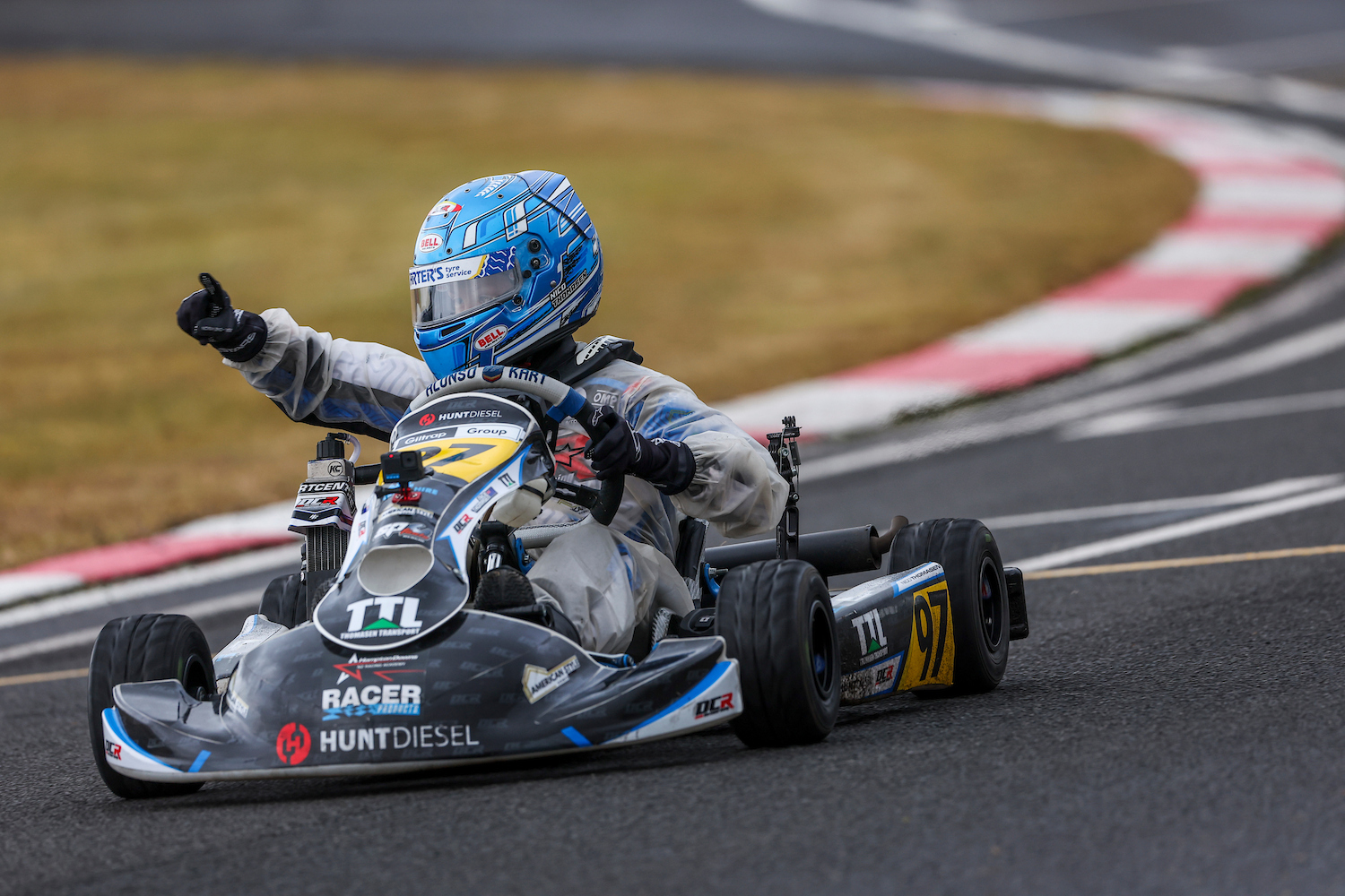 Nico Thomasen giving a thumbs up while driving his number 97 kart on a wet track